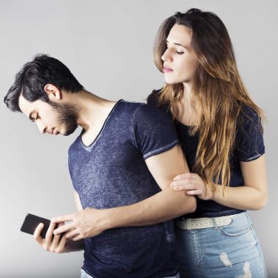 Young man with mobile phone and his girlfriend trying to see what he does behind him